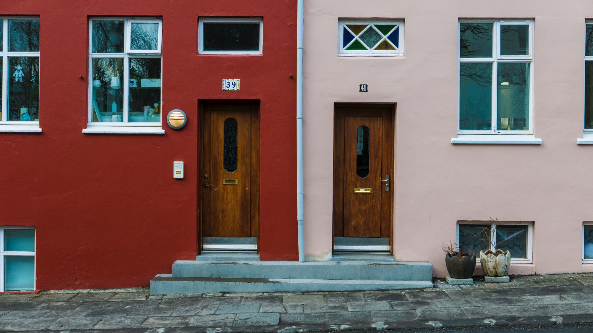 Neighbouring red and pink homes with front doors opening onto the street