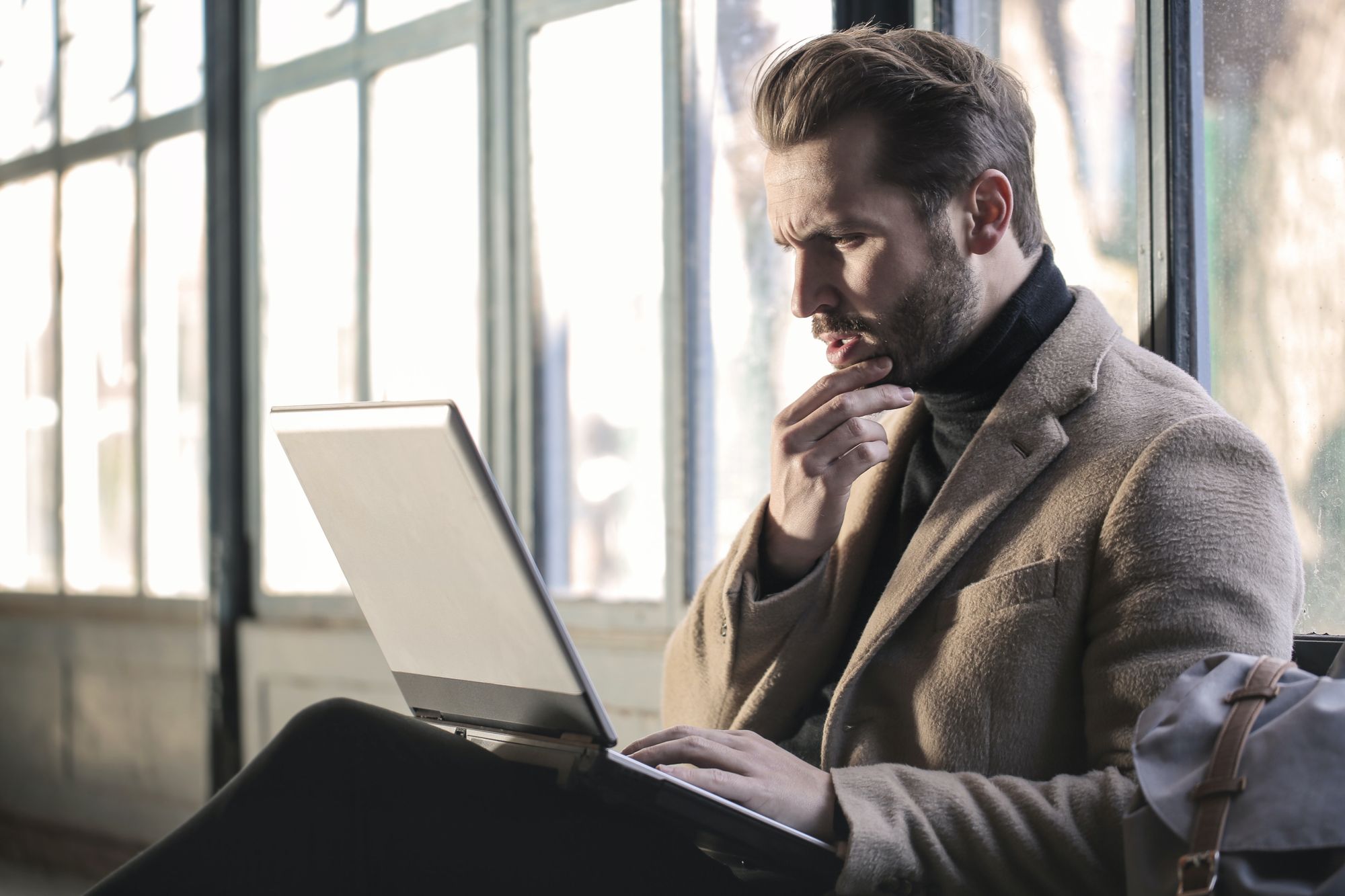 Man looking at a laptop beside a large window