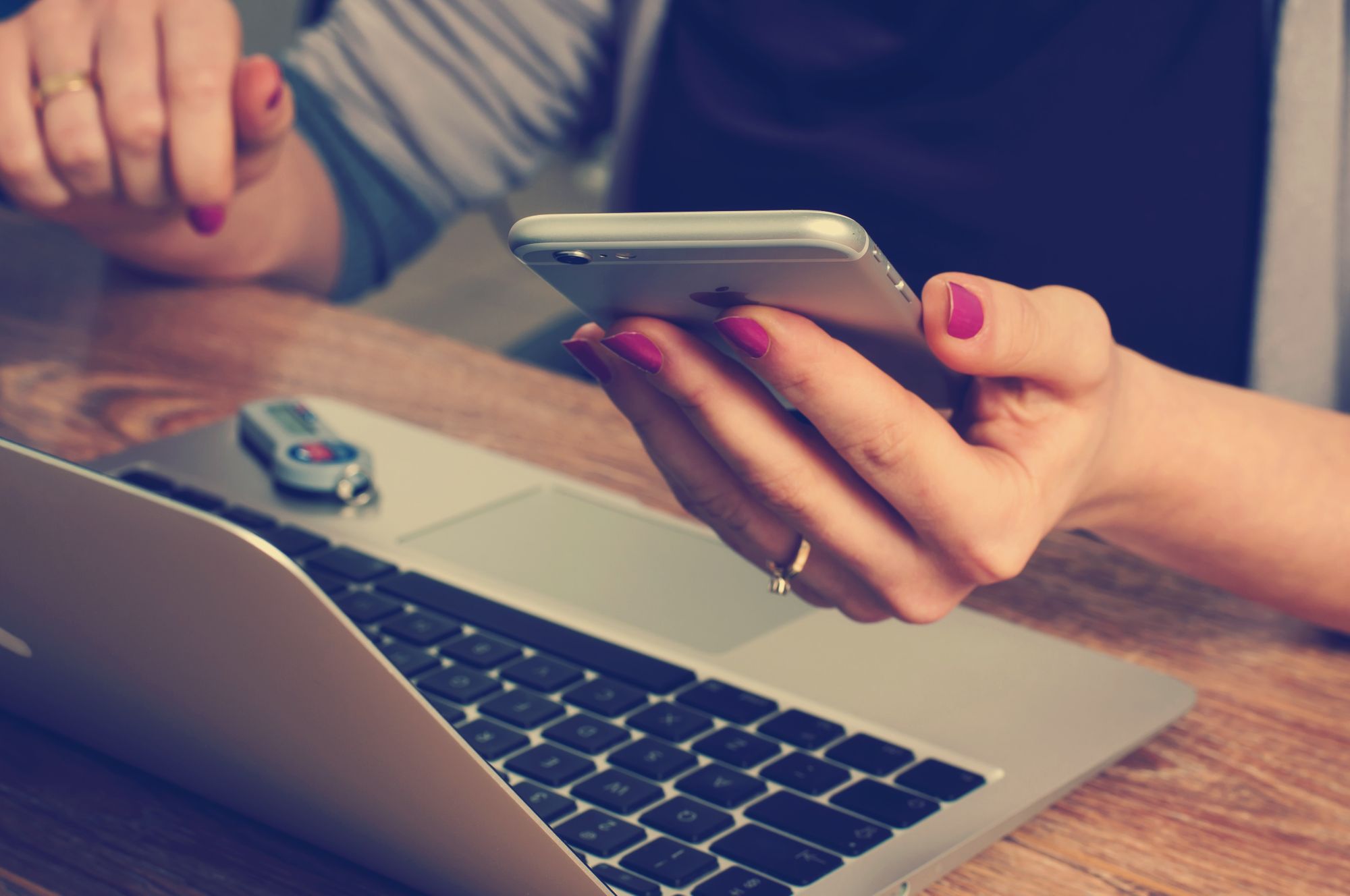 Person using a smartphone beside a laptop and house keys